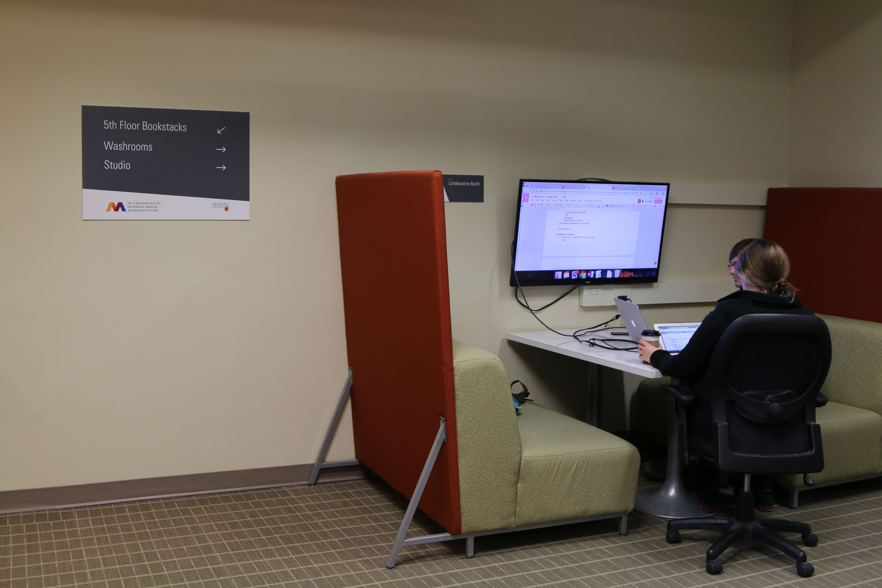 Image shows a collaborative booth with table, staff member and TV monitor